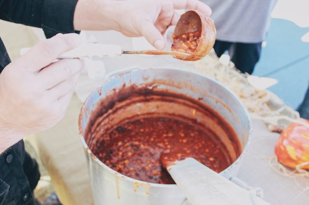 a person scoops some chili into a ladle and transfers it into a sample cup at an outdoor chili cook t20 XxkxYb