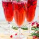 Three pomegranate mimosas in champagne flutes garnished with pomegranates and rosemary