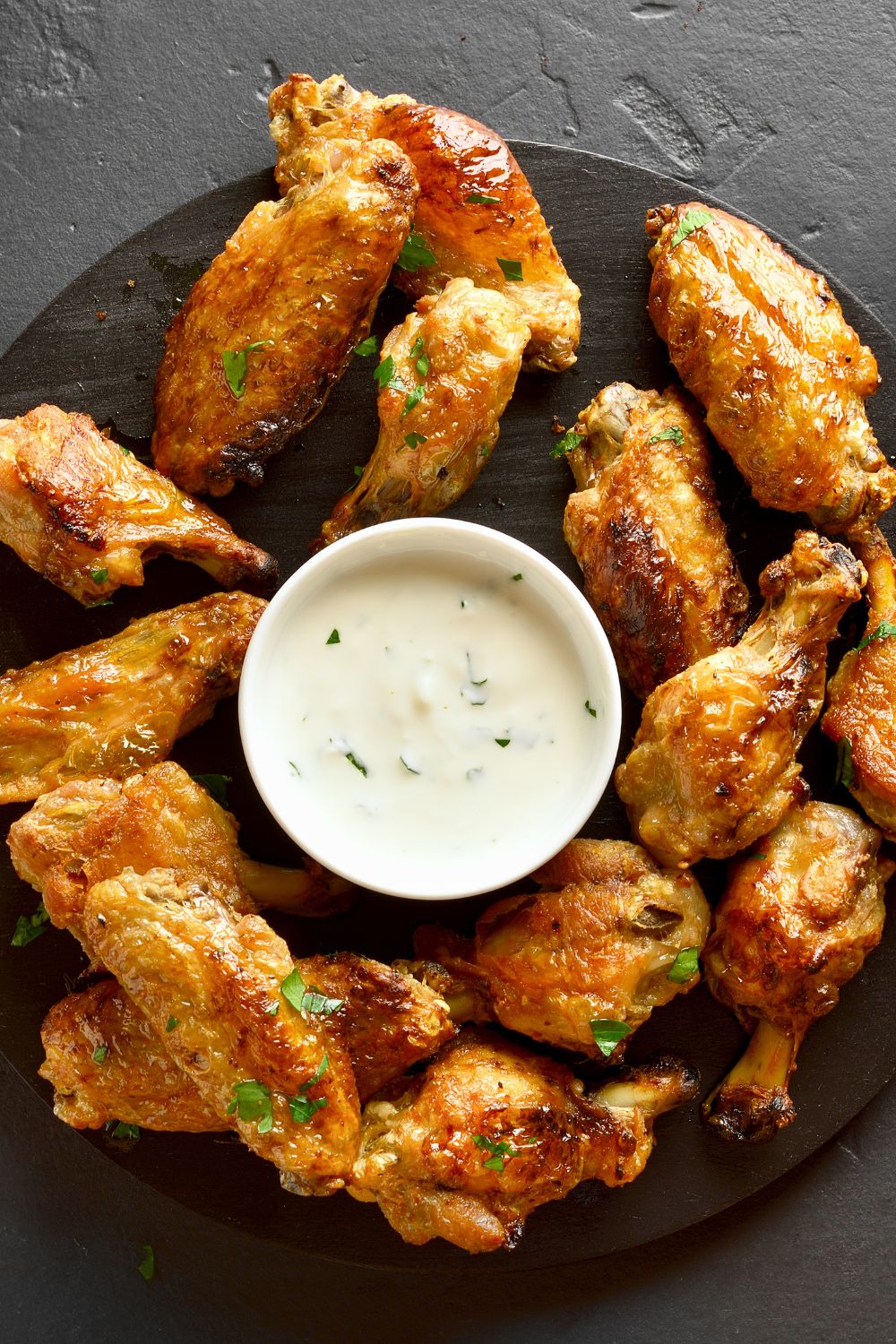 A black plate filled with pickle brined chicken wings with ranch dressing in the middle