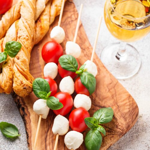 a wooden serving board with caprese salad skewers and breadsticks