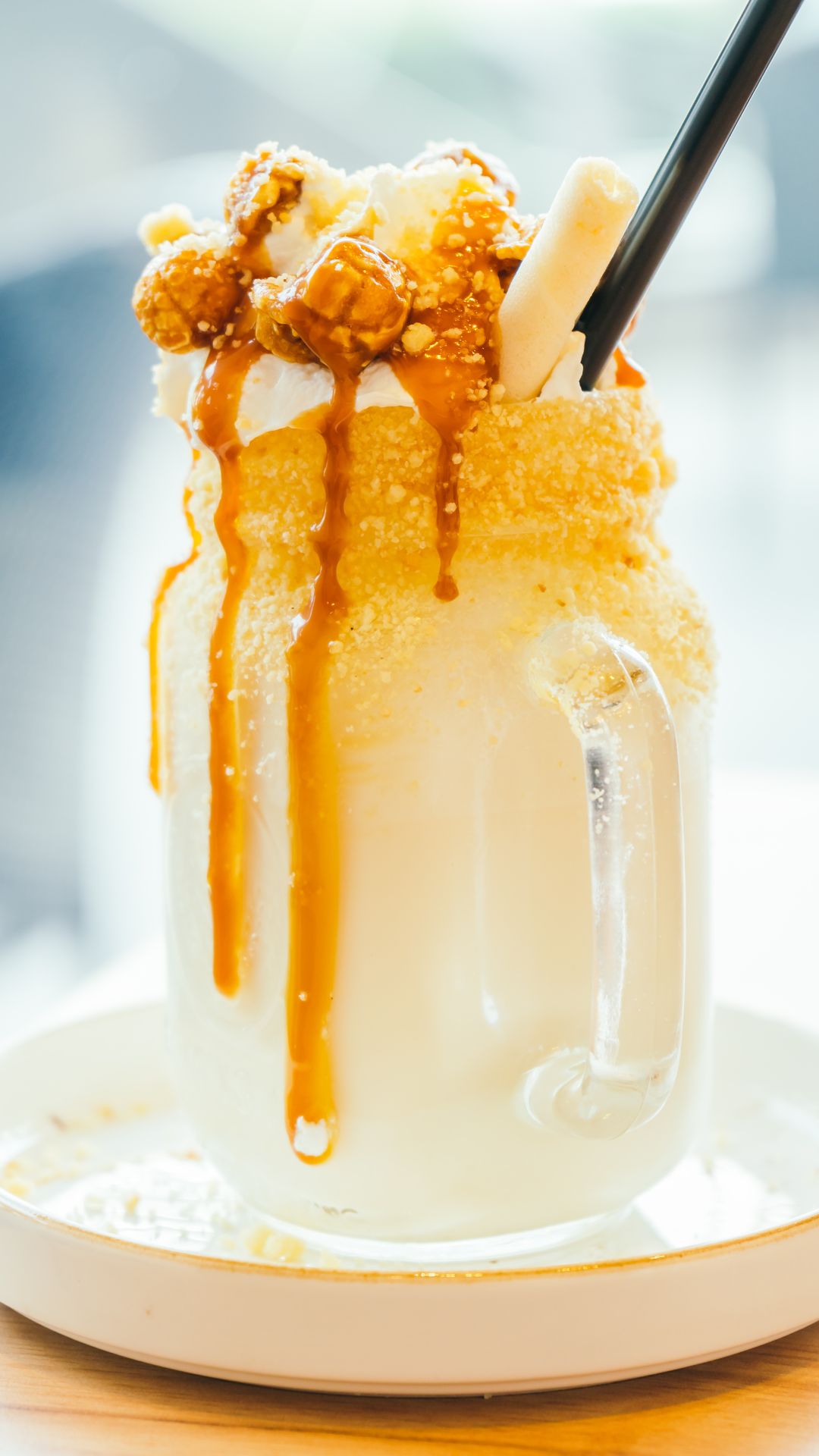 A boozy caramel milk shake in a glass jar with caramel popcorn and a straw