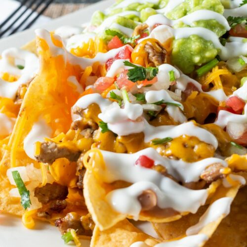 Individual nachos on a plate topped with sour cream and guacamole