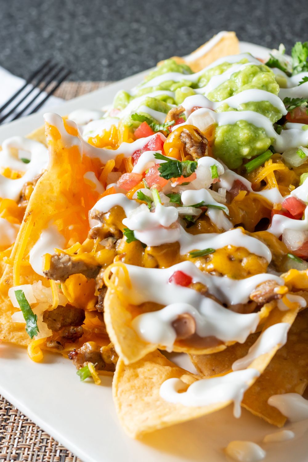 Individual nachos on a plate topped with sour cream and guacamole