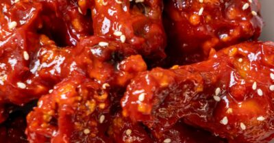 An overhead shot of korean gochujang wings sprinkled with sesame seeds on a white plate.