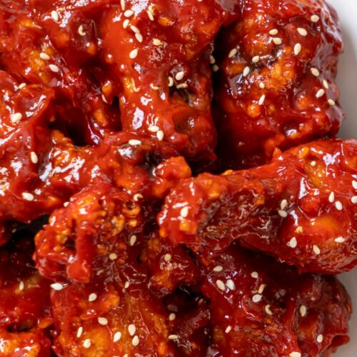 An overhead shot of korean gochujang wings sprinkled with sesame seeds on a white plate.