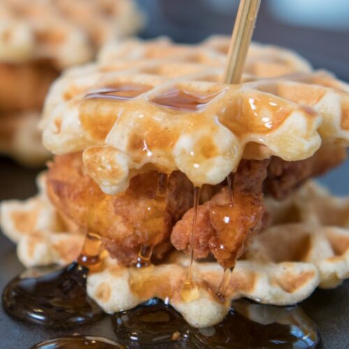 mini chicken and waffles on a black plate with honey butter and a toothpick