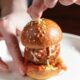 Hands holding a mini meatball slider with sesame seeds on the bun