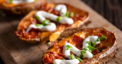 Mini potato skins topped with bacon, green onion and sour cream on a wooden serving board.