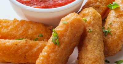 A plate filled with crispy and golden mozzarella sticks with marinara sauce on the side