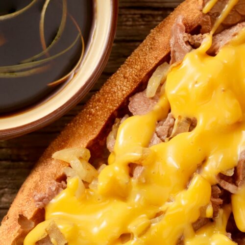 A prime rib sandwich on a toasted bun topped with melted cheese and served with au jus
