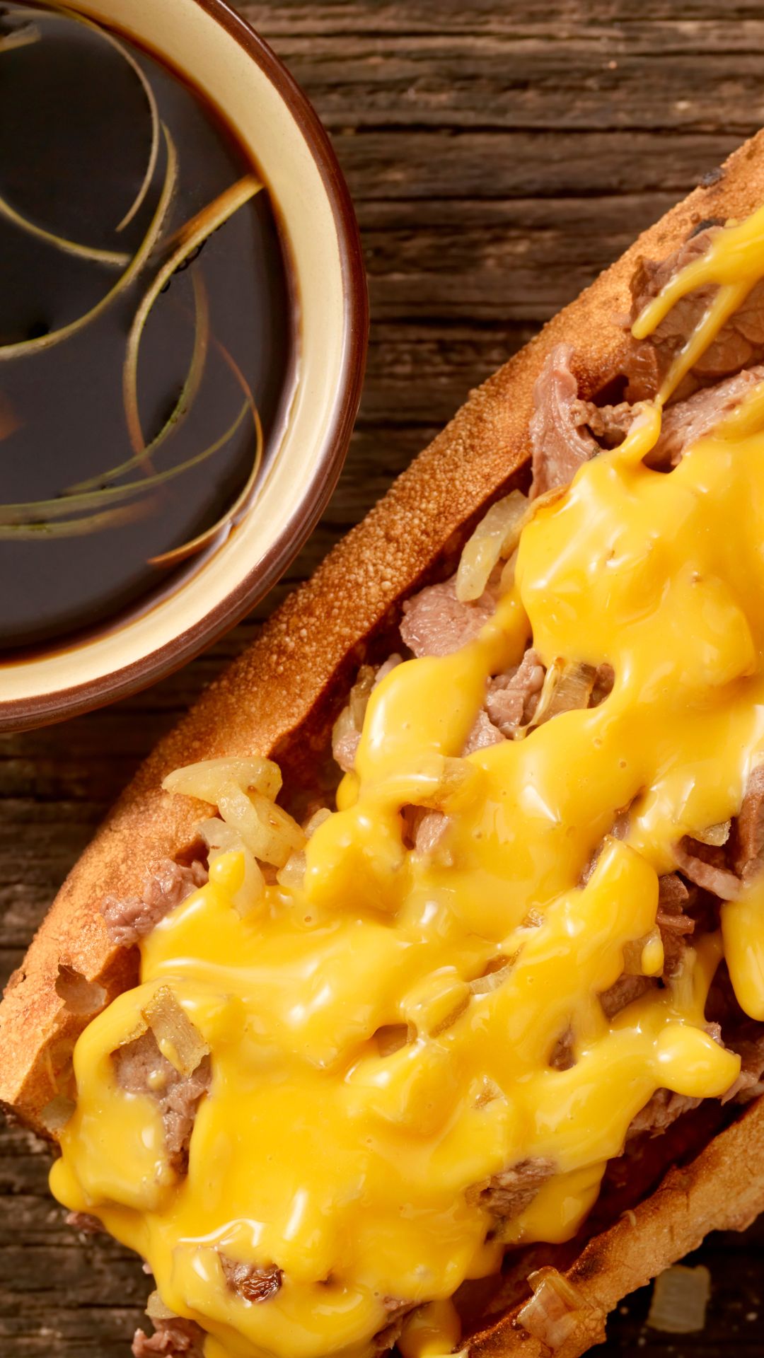 A prime rib sandwich on a toasted bun topped with melted cheese and served with au jus