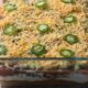 Race day dip in a glass baking dish topped with sliced jalapeno peppers