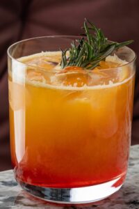 An azalia cocktail in a glass with rosemary on top