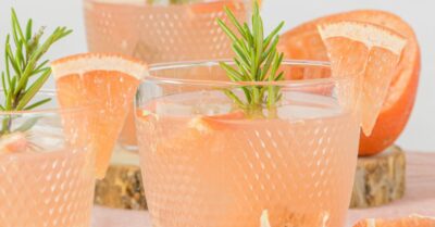 Three plastic cups filled with a grapefruit bourbon rosemary punch with slices of grapefruit and rosemary sprigs in the cups