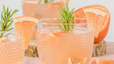 Three plastic cups filled with a grapefruit bourbon rosemary punch with slices of grapefruit and rosemary sprigs in the cups