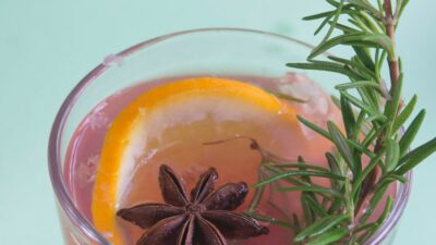 Bourbon rosemary punch in a plastic cup with an orange slice, rosemary sprig and anise.