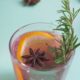 Bourbon rosemary punch in a plastic cup with an orange slice, rosemary sprig and anise.