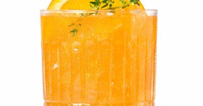 An orange electric skrewdriver cocktail in a glass with an orange slice and thyme