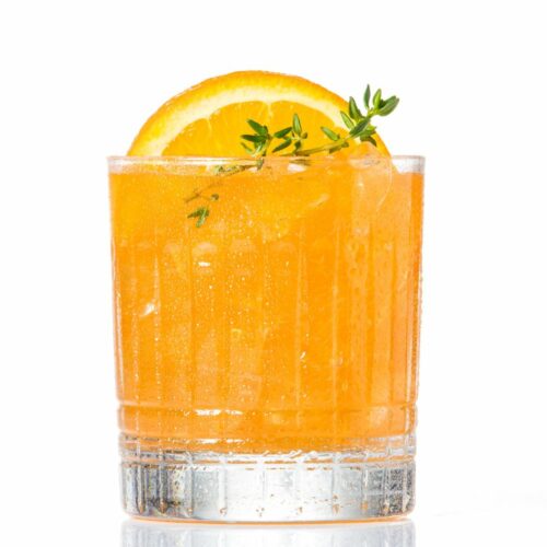 An orange electric skrewdriver cocktail in a glass with an orange slice and thyme
