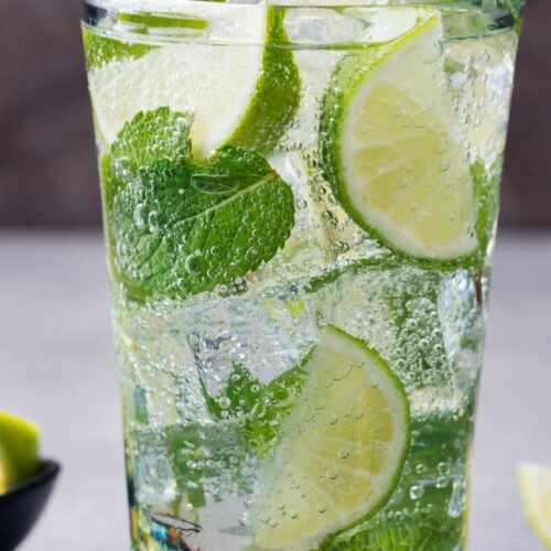 A glass filled with mojito, limes and mint leaves