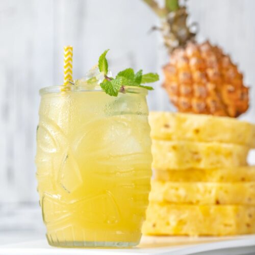 A glass jar filled with pineapple party punch with sliced pineapple in the background