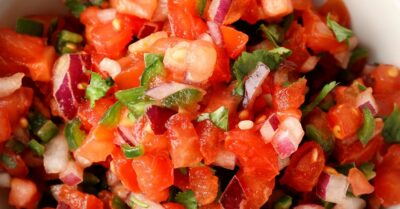 A bowl of tennis team salsa filled with chopped tomatoes red onion, and cilantro