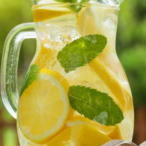 A glass pitcher filled with vodka mint lemonade, lemon slices, and mint leaves.