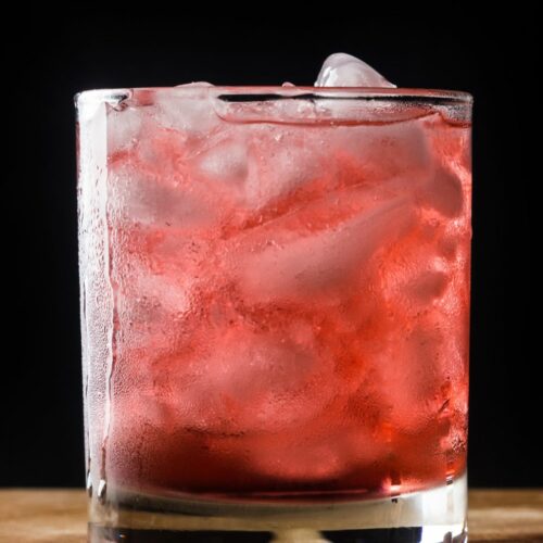 A blackberry cocktail in a glass filled with ice