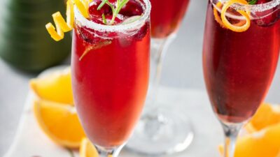 Three orange cranberry bellini's in champagne flutes garnished with orange and rosemary