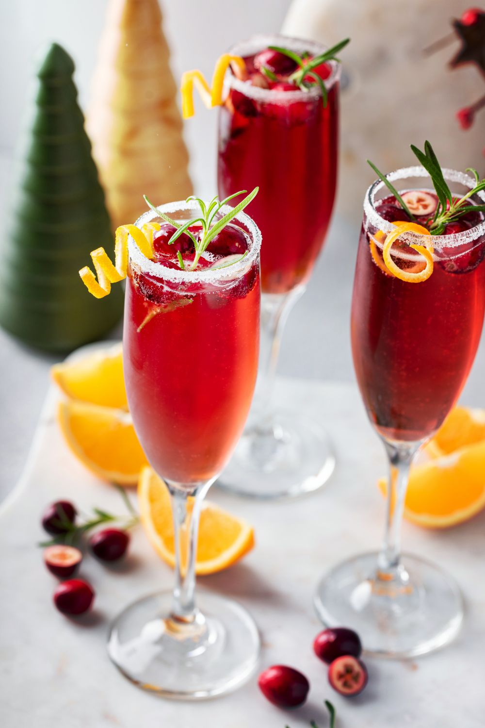 Three orange cranberry bellini's in champagne flutes garnished with orange and rosemary