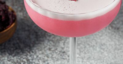 A pink habanero hibiscus sour in a coup glass with egg white foam on top