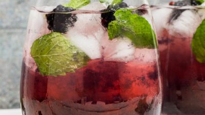 A hats off julep cocktail in a glass garnished with blackberries and mint