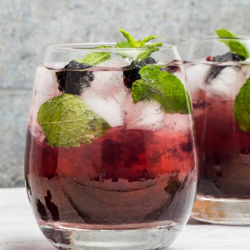 A hats off julep cocktail in a glass garnished with blackberries and mint