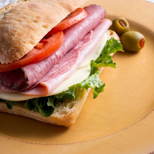 Mario Carbone's Italian sandwich on a plate with sliced tomato and lettuce