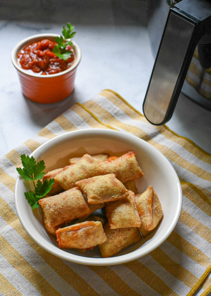 A bowl filled with air fryer pizza bites with marinara sauce in the background