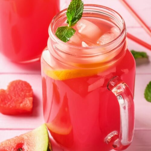 Pink watermelon moonshine in a mason jar with sliced watermelon around it