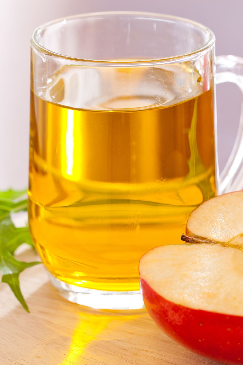 a glass of apple spiked cider next to a cut apple