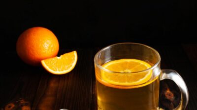 Spiked orange tea in a glass tea cup with orange.