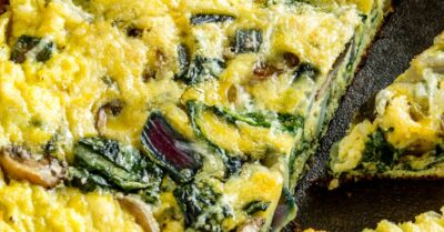 A grilled frittata in a cast iron skillet with spinach showing.