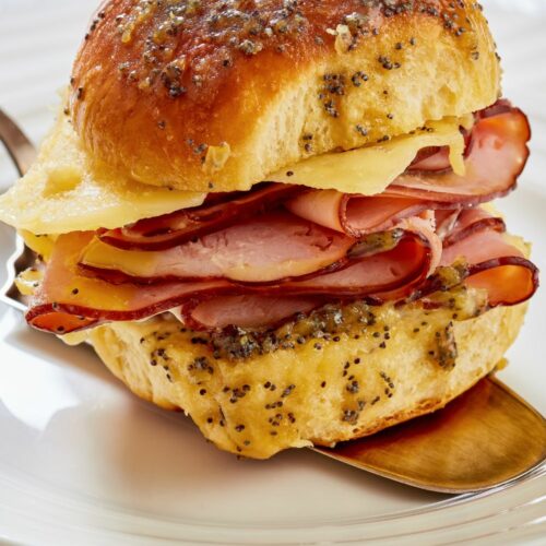 A hawaiian roll breakfast slider with ham and cheese on a plate.