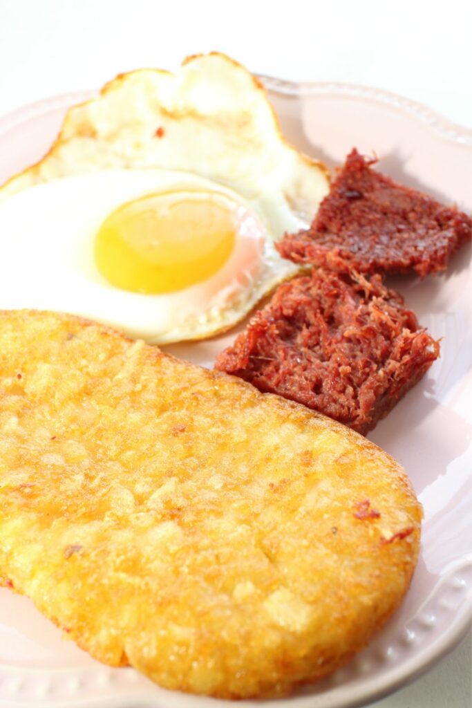 A sunny side up egg and corned beef next to a crispy hash brown.