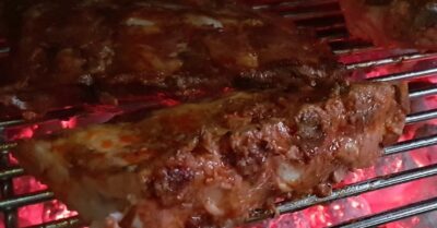 Two racks of bbq ribs on a charcoal grill being cooked over hot coals.