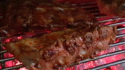 Two racks of bbq ribs on a charcoal grill being cooked over hot coals.