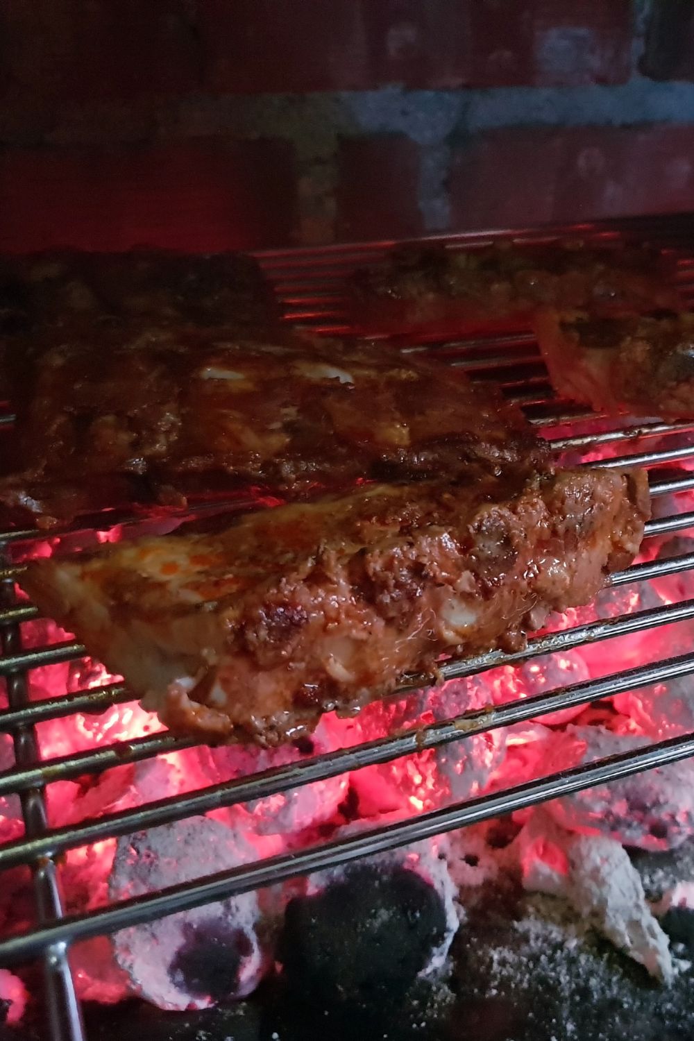 Two racks of bbq ribs on a charcoal grill being cooked over hot coals.