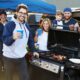 Friends around a grill smiling at a football tailgate party.