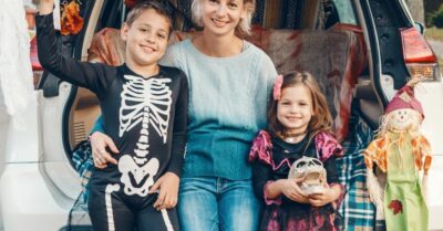 A mother and her son and daughter sitting in a car decorated for a trunk or treat halloween tailgate.