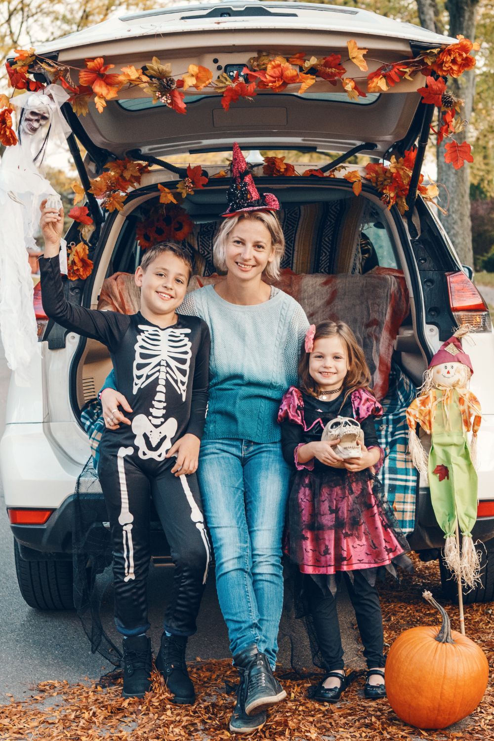 A mother and her son and daughter sitting in a car decorated for a trunk or treat halloween tailgate.