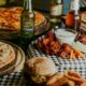 A spread of pizzas, wings, burgers and beer for a super bowl party.