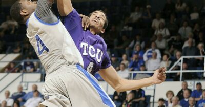 A college basketball player trying to dunk with another defending them.