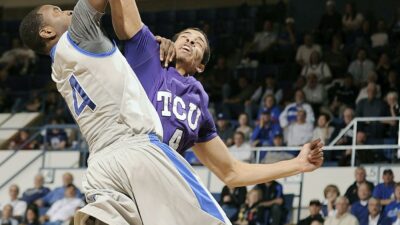A college basketball player trying to dunk with another defending them.